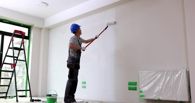 Builder paints wall with long roller. Concept of repair and redecoration