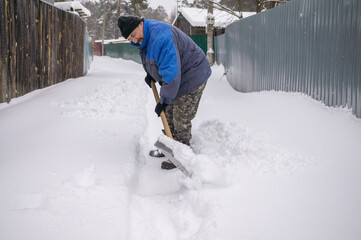 man shovels snow in the yard in winter. Clearing a road in a country village or village