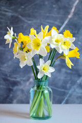 A vase of daffodils is on a table with a grey background.