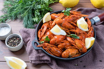 cooked crawfish in black saucepan with lemons and spices on wooden background