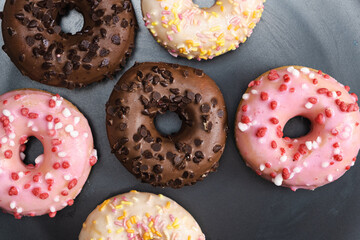 Lots of little donuts with white, pink and chocolate glaze on a black plate, top view