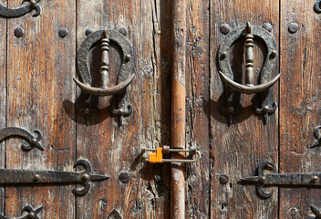 old wooden door with decorative wrought iron bolts and knockers and with a modern padlock
