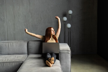 Business young woman wearing white shirt sitting on sofa with laptop raising her arms above her...