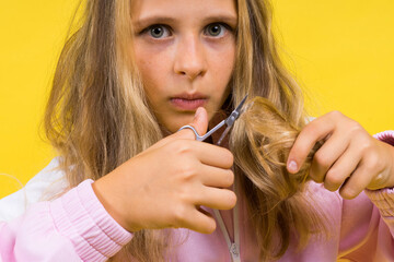 Child adorable girl hairdresser cutting long blonde hair with metallic scissors on yellow