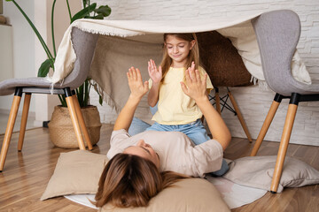 A mother with her daughters plays in the living room  in a tent built with blanket. Concept of: family, fun, educational, magic, creativity. © Julija