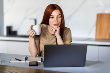 Young Woman working from home at laptop on kitchen counter