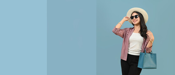 Smiling Asian woman in summer hat and sunglasses isolated on blue background with copy space for your graphic design or banner 