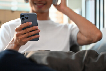 Selective focus on hand. Smiling man using smart phone and relaxing on couch. People, Technology and lifestyle concept