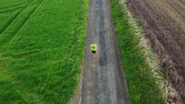 Athl&egrave;te courant sur une petite route de campagne entre les champs. Personne qui court seul sur une petite route goudronn&eacute;e