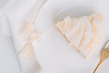 White cheesecake with coconut flavor on plate with fork on white background with napkin.