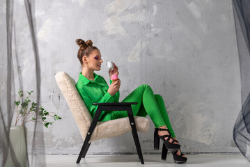 Extraordinary girl in green suit with cup of coffee and muffin.Model with hairstyle and bright makeup on gray background