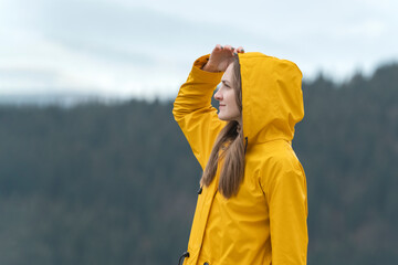 Portrait of young woman in yellow jacket in nature looks into the distance. Forest on background. Side view.