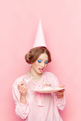 Stylish, beautiful, young girl with makeup opening her birthday cake against pink studio...