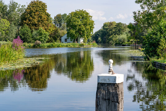 A bollard in the water of the Kerkvaart and a small white house hidden in the greenery near Alphen aan den Rijn, the Netherlands