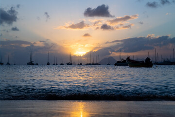 Sunset panorama at the beach of Saint Anne in the south of french overseas island Martinique. Sailing boats anchoring in the bay near “Le Marin“, a popular spot for yachtsmen in the Caribbean sea.