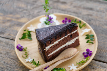 Chocolate cake. Slice of chocolate fudge with butter cream cake. Tasty homemade soft and delicious chiffon cake on table wooden plate with sweet purple flower on wooden table. Bakery dessert concept.