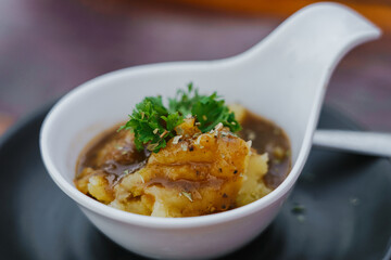 Delicious mashed potatoes with gravy sauce parsley on top in white plate on table.