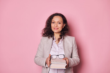 Attractive multi-ethnic middle aged woman, school teacher librarian smiling at camera, holding book...