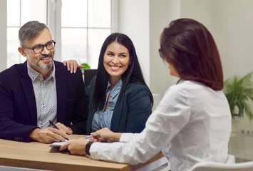 Fotobehang Portrait of an attractive, happy man and two beautiful, young women talking in a business setting, sitting at a desk in the office. Familiarization and signing of documents during working hours. © Studio Romantic