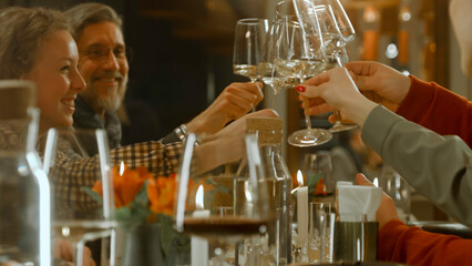 Close up shot of waiter pouring red wine from the bottle into the glass in restaurant. People clink glasses, celebrate birthday, spend weekend evening in modern gastro cafe. Public catering concept.