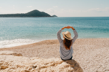 Woman wearing a hat sitting on the rock watching beautiful turquoise sea and an island.