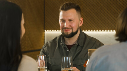 Caucasian man sits in modern gastro cafe, eats delicious dish and talks to friends. Group of people celebrate birthday, have family dinner, spend weekend together in restaurant. Public eating concept.