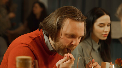 Close up shot of man eating delicious dish, smiling, talking with friends in modern gastro cafe. He has birthday party, family dinner, spends evening in restaurant. Concept of public eating. Zoom in.