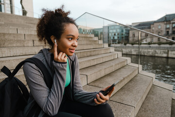 Smiling african girl using mobile phone while sitting on stairs