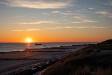 Sunset photo from the dunes of the North Sea coast and the beach with a boat and the polders and windmills on the horizon