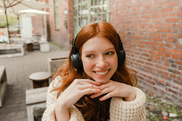 Portrait of redhead girl listening music with headphones while sitting outdoors