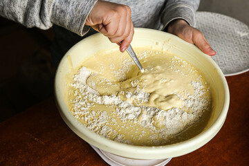 the process of making dough with the hands of a child in a yellow toe with a spoon on a dark wooden table.