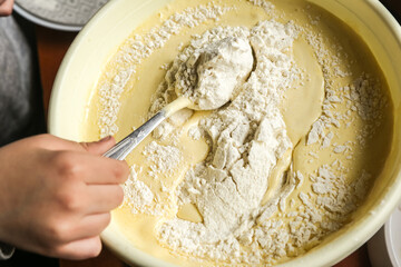 the process of making dough with the hands of a child in a yellow toe with a spoon on a dark wooden table close-up.