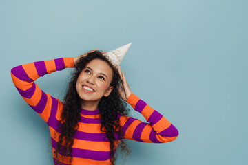 Beautiful girl wearing party hat smiling while posing isolated over blue background