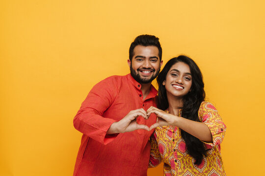 Indian couple showing heart gesture with fingers isolated over yellow background