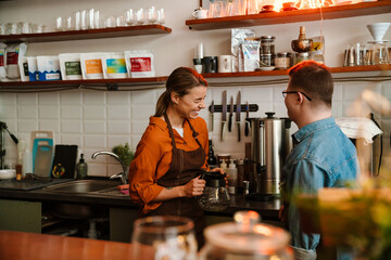 Woman training man with down syndrome to work as barista in coffee shop