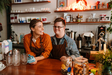 Man with down syndrome and his female colleague smiling while standing at counter in coffee shop - 593902619
