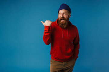 Naklejka premium Excited man pointing finger away at copy space isolated over blue background
