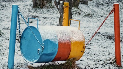 Colorful metal barrel hanging with chains in poles and snow on it