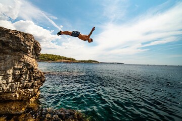 Guy jumping into the sea with a cloudy blue sky in the background in Croatia