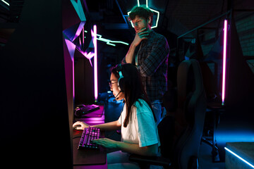 Friend of asian girl watching her playing video game in cybersport club