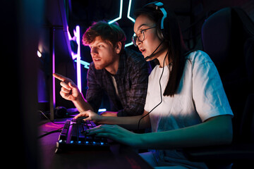 Friend of asian girl watching her playing video game and assisting her in cybersport club © Drobot Dean