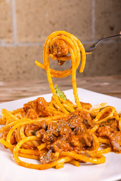 Piatto di spaghetti con sugo di soffritto napoletano fatto con  interiora di maiale cotte nel sugo di pomodoro e guarnito con basilico fresco e formaggio servito in un ristorante