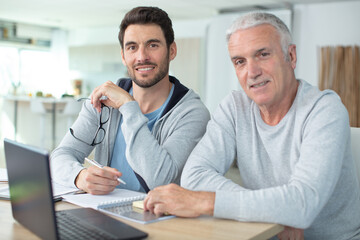 adult son helping senior father with computer at home