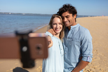 young couple taking selfie with selfie stick on beach