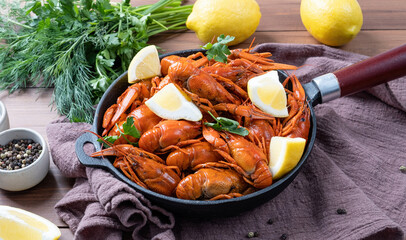 cooked crawfish in black saucepan with lemons and spices on wooden background