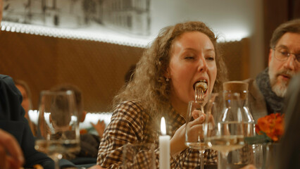 Close up shot of woman eating and enjoying tasty dish, talking with friends in modern gastro cafe. She celebrates birthday, has family dinner, spends evening in restaurant. Concept of public catering.