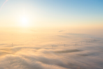 Windmills, windturbines above of the fog clouds with sunrise behind