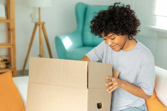 African girl unpacking delivery looking in box. Happy woman opening carton box. Female getting parcel looking at delivered goods items. Satisfied client positive feedback quick express deliver