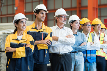 Group of male and female factory workers standing together with crossed arms and smiling in industry factory, wearing safety uniform and helmet. Factory workers working in factory