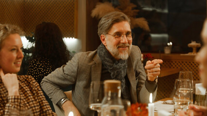 Mature man sits in modern gastro cafe with friends. He celebrates birthday, has family dinner, spends weekend evening in restaurant. The waitress brings dishes on table. Concept of public catering.